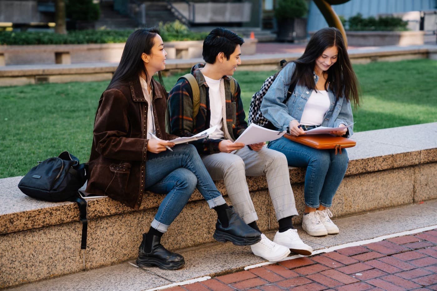 Three students sitting outdoors reviewing their coursework